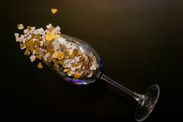 Golden Paper Hearts spreadin from a Wine Glass on a Black Background