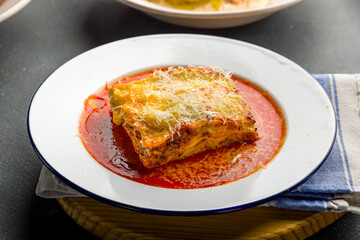 lasagna Bolognese on a plate with tomato sauce on grey concrete table