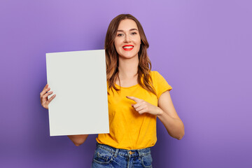 Fototapeta na wymiar caucasian young woman holding a white poster in her hands wearing a yellow t-shirt and isolated on a lilac background. mockup