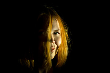 A middle-aged woman smiles mysteriously in the dark. Dark background. A woman of forty years old. Red hair.