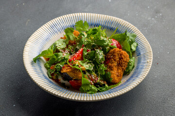 Salad with baked aubergines, feta cheese and red tomatoes with greens on grey concrete table