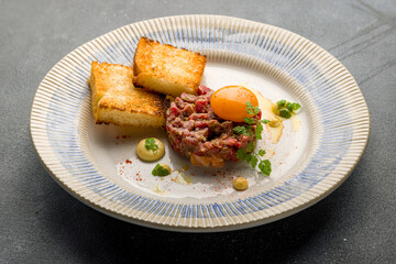 Tartare from beef with egg and bread on plate on grey concrete table