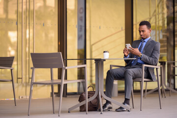 Black businessman using phone at coffee shop restaurant outdoors