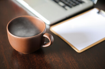 brown cup of coffee, with hot steam, on the work desk