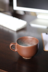 brown cup of coffee, with hot steam, on the work desk