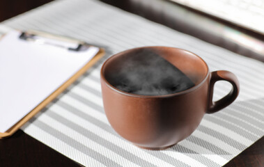 brown cup of coffee, with hot steam, on the work desk
