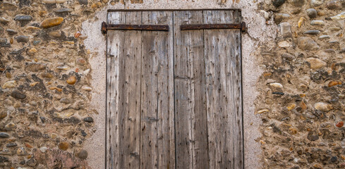 Vintage old wooden shutters on the stone wall background. Wooden brown window frame. Window with shutters in the house close-up.