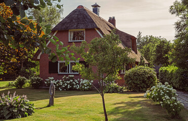 View of typical houses of Giethoorn, Netherlands. The beautiful houses and gardening. Landscape view of famous Giethoorn village with canals and rustic thatched roof houses in farm area.
