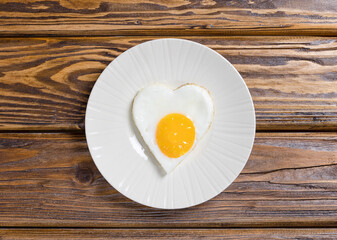 Fried eggs in the shape of a heart on a white plate and a wooden background for a healthy breakfast. The concept of Valentine's Day. Top view.
