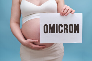 Pregnant woman holds a sheet of paper with the text of the new variant coronavirus Omicron, blue background