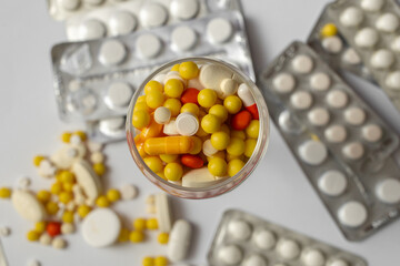 Yellow, red, orange capsules and tablets in a container on a white background.