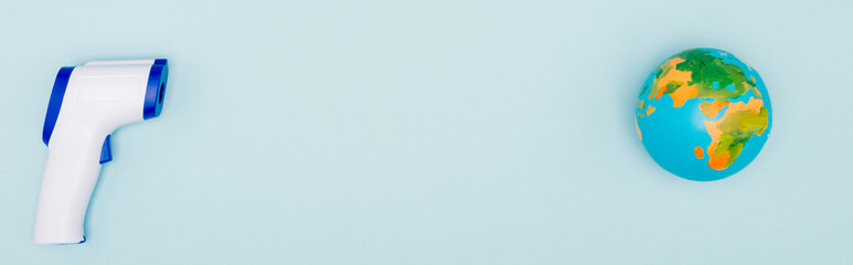 top view of globe near non-contact thermometer on blue background with copy space, banner.