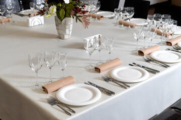 Close up new white porcelain tableware plates on white tablecloths and empty wine glasses ready for dinner.