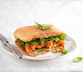 Smoked salmon sandwich and fresh spinach, arugula leaves, on a light background. Delicious brunch, breakfast.