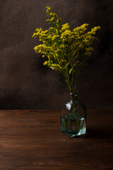 Solidago flower in a blue glass vase. Vertical orientation, brown background, low key, copy space.