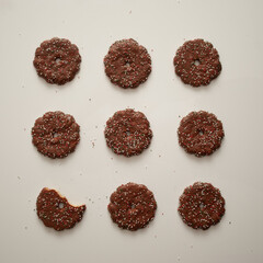 Top view of decorated chocolate cookies, one bitten cookie on white background, concept of holiday celebration. Pattern, flat lay.
