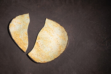 A hand-made ceramic plate, broken in half, lies on a textured, dark background. Deconstruction concept, top view, close-up, copy space.