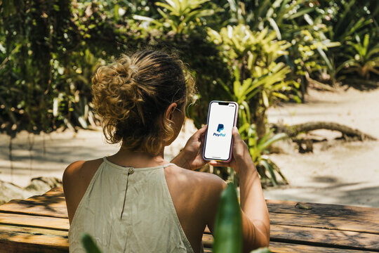 Girl in the park holding a smartphone with PayPal app on the screen. Rustic wooden table. Rio de Janeiro, RJ, Brazil. January 2022
