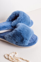 Blue women's home slippers and pearl necklace. Fur close up. Comfortable shoes for home
