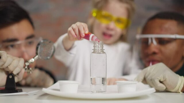 Joyful girl drips red liquid into bottle with tutors in lab