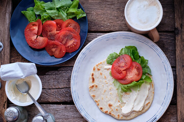 Flatbread with sauce, tomato, lettuce. Wooden background, top view