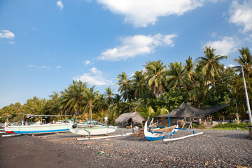 Colorful outrigger fishing boats on a shady beach in Bali Indonesia with sunny blue sky overhead