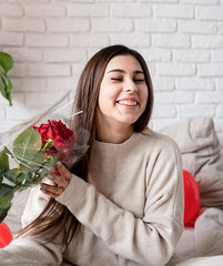 Young beautiful woman sitting in the bed celebrating valentine day holding red roses