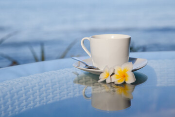Cup of coffee and frangipani flowers on the table in the morning