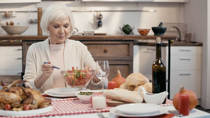 Obraz na płótnie Canvas senior woman holding bowl of vegetable salad near roasted turkey and red wine on table.
