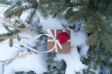 gift box and red glass heart in the snow on spruce branches. valentine's day card