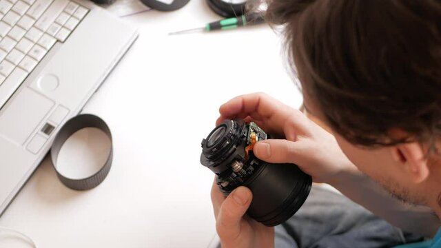 man repairs camera lens, autofocus motor, tools. master thinks