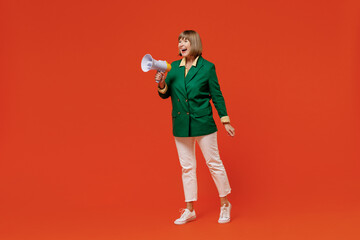Full body elderly caucasian woman 50s wearing green classic suit hold scream in megaphone announces discounts sale Hurry up isolated on plain orange color background People business lifestyle concept