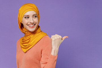 Smiling young arabian asian muslim woman in abaya hijab yellow clothes pointing thumb finger back...