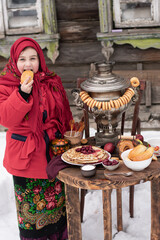A joyfool girl bites pie in traditional clothes with a stack of pancakes, samovar. Maslenitsa .