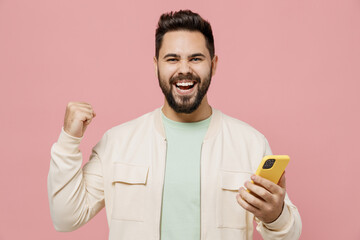 Young smiling happy man 20s wearing trendy jacket shirt hold in hand use mobile cell phone browsing...