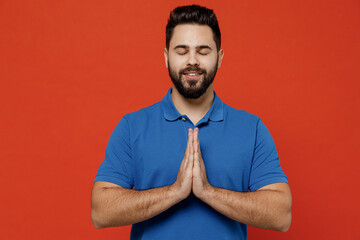 Young smiling happy caucasian man 20s wear basic blue t-shirt hold hands folded in prayer gesture,...