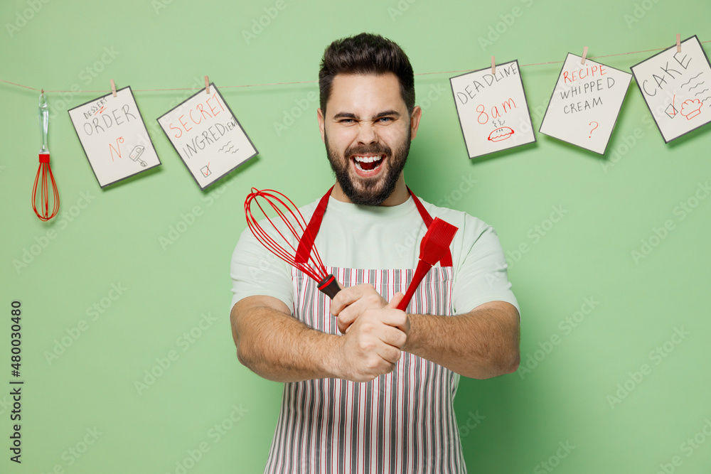 Wall mural young expressive happy cheerful male chef confectioner baker man in striped apron hold whisk silicon