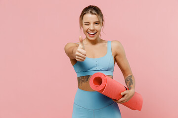 Young strong sporty athletic fitness trainer instructor woman wear blue tracksuit spend time in home gym show thumb up gesture blink isolated on pastel plain pink background. Workout sport concept