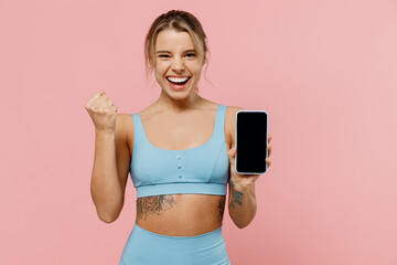 Young sporty athletic fitness trainer instructor woman wear tracksuit spend time in home gym hold mobile cell phone blank screen area do winner gesture isolated on plain pink background Sport concept.