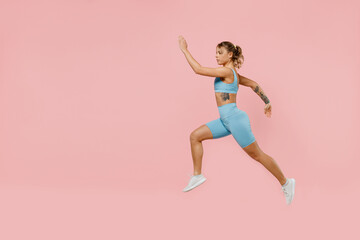Fototapeta na wymiar Full body young strong sporty athletic fitness trainer instructor woman wearing blue tracksuit spend time in home gym jump high isolated on pastel plain light pink background. Workout sport concept.