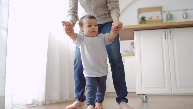 Asian Little toddler boy learning to walk, Mother support and care, Young Mom assisting son make first steps at home