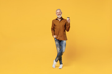 Full size body length calm elderly gray-haired bearded man 40s years old wear brown shirt hold takeaway delivery craft paper brown cup coffee to go isolated on plain yellow background studio portrait