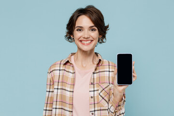 Fototapeta premium Young smiling happy fun woman 20s wearing casual brown shirt hold in hand use mobile cell phone with blank screen workspace area isolated on pastel plain light blue color background studio portrait