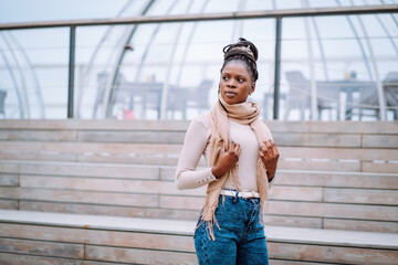 Outside portrait of Afro-American woman in beige scarf and roll-neck sweater with long afro braids gathered in bun.