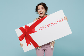 Young smiling happy woman 20s in casual brown shirt hold big gift certificate coupon voucher card for store isolated on pastel plain light blue background studio portrait. People lifestyle concept