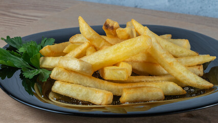 French fries on black dish on parchment background. Tasty golden french fries on a plate.