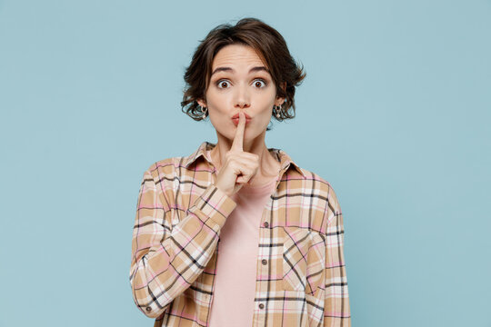 Young secret woman 20s wearing casual brown shirt says hush be quiet with finger on lips shhh gesture isolated on pastel plain light blue color background studio portrait. People lifestyle concept