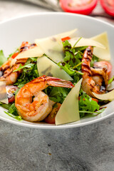 Arugula with shrimps and parmesan on plate on grey concrete table macro close up