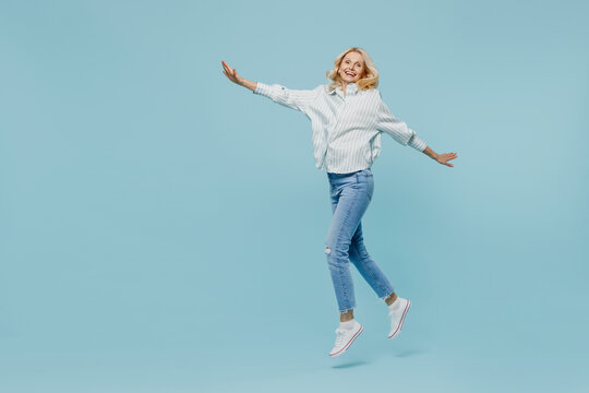 Full Body Elderly Woman 50s Wearing Casual Striped Shirt Looking Camera Jump Hilg With Outstretched Hands Like Fly Run Isolated On Plain Pastel Light Blue Color Background. People Lifestyle Concept