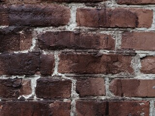 brick background with brown blocks and dark burnt coating close-up, brickwork texture with uneven surface, masonry fragment with dark shabby bricks